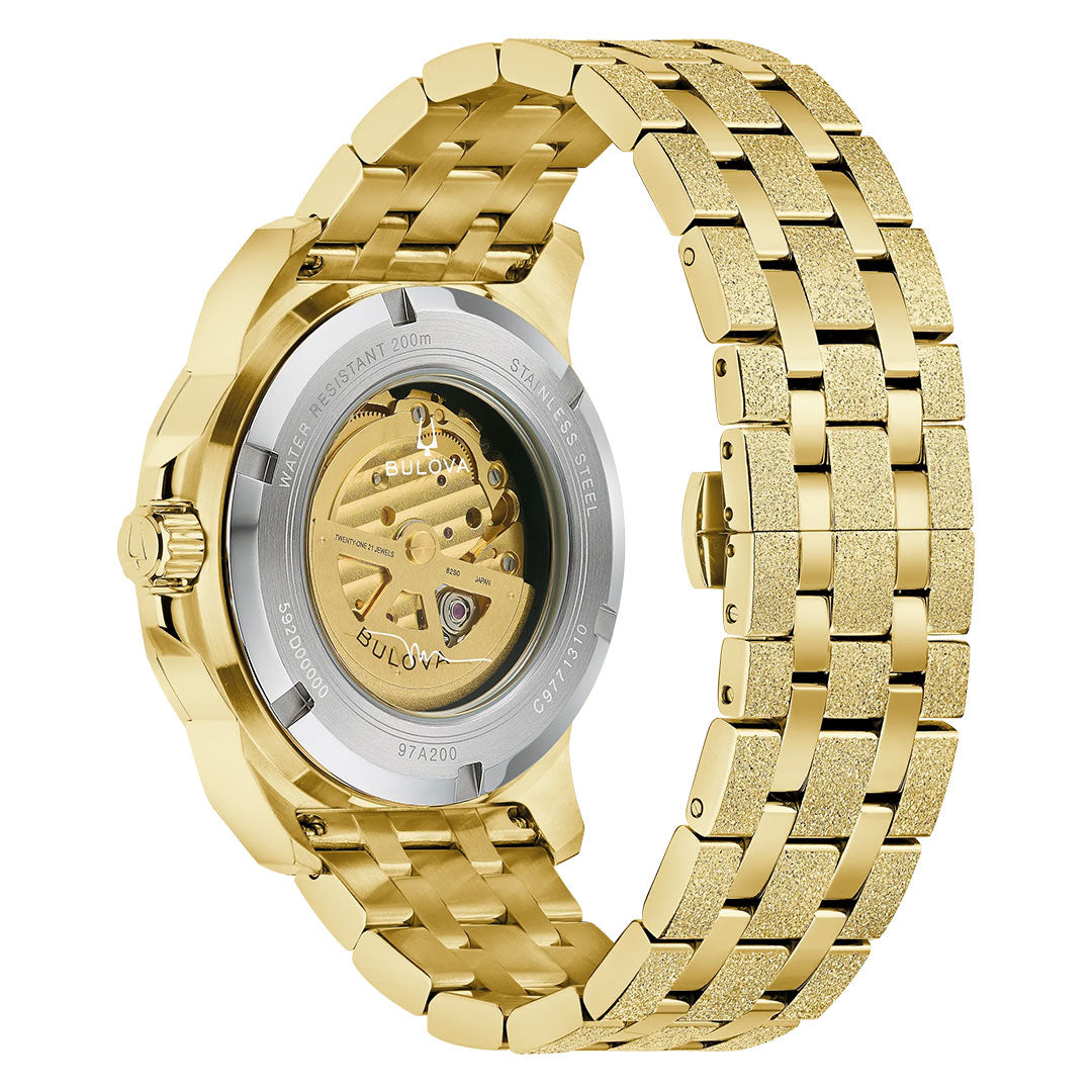 The Bulova Marine Star Marc Anthony Automatic 44mm Watch is shown from the back, displaying its stainless steel case and transparent caseback. The watch features a gold-tone bracelet with polished and textured links that complete its bold look.