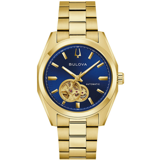 The Bulova Surveyor Automatic 39mm Watch is a gold men’s timepiece featuring a striking blue dial with gold hour markers and an open heart mechanical movement visible at the 8 o’clock position. It is finished with a matching gold metal band.