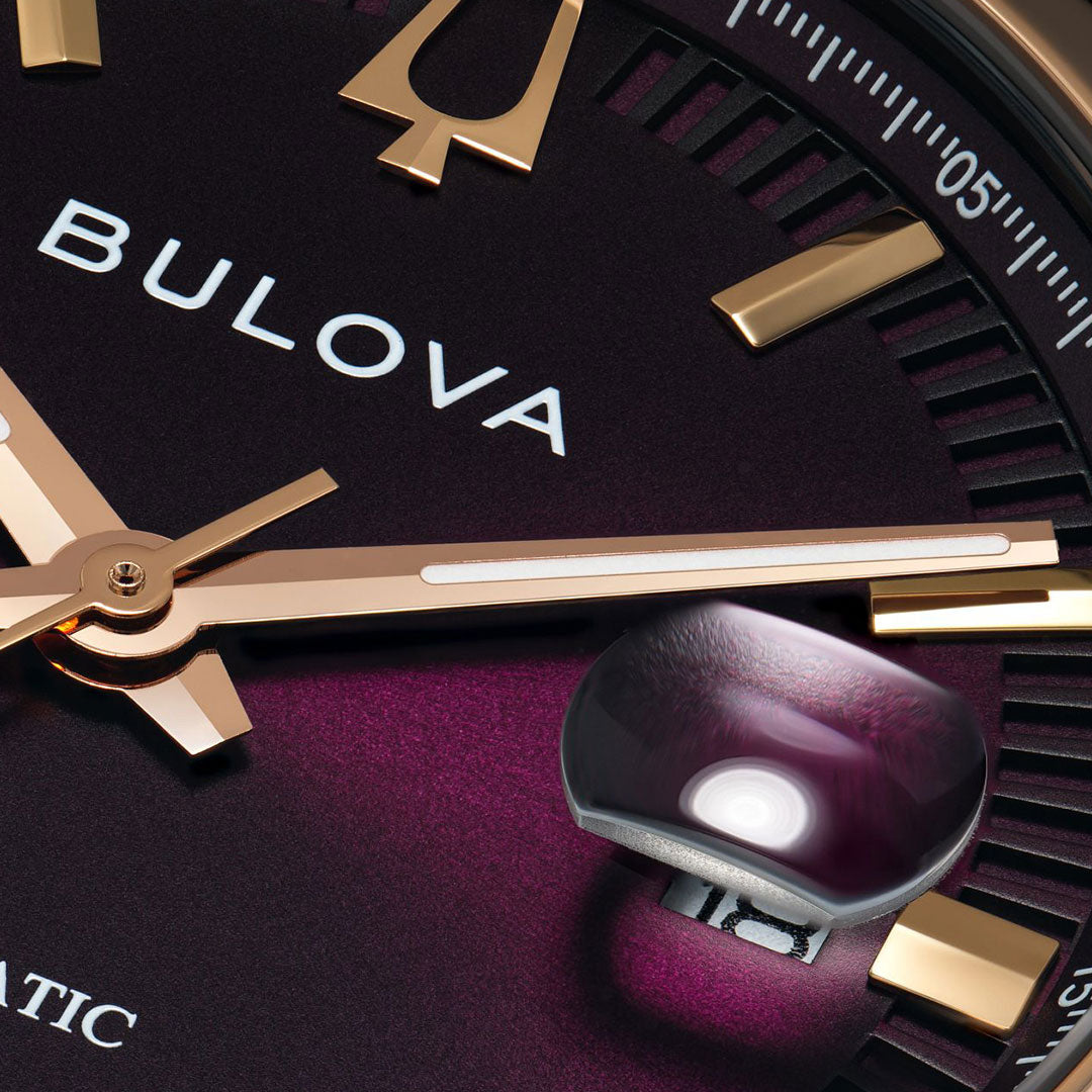 Close-up of the Bulova Surveyor Automatic 39mm Watch, featuring a deep purple face, rose gold-tone markers and hands, and a magnified date window. The texture and shine of this Bulova piece are clearly visible.