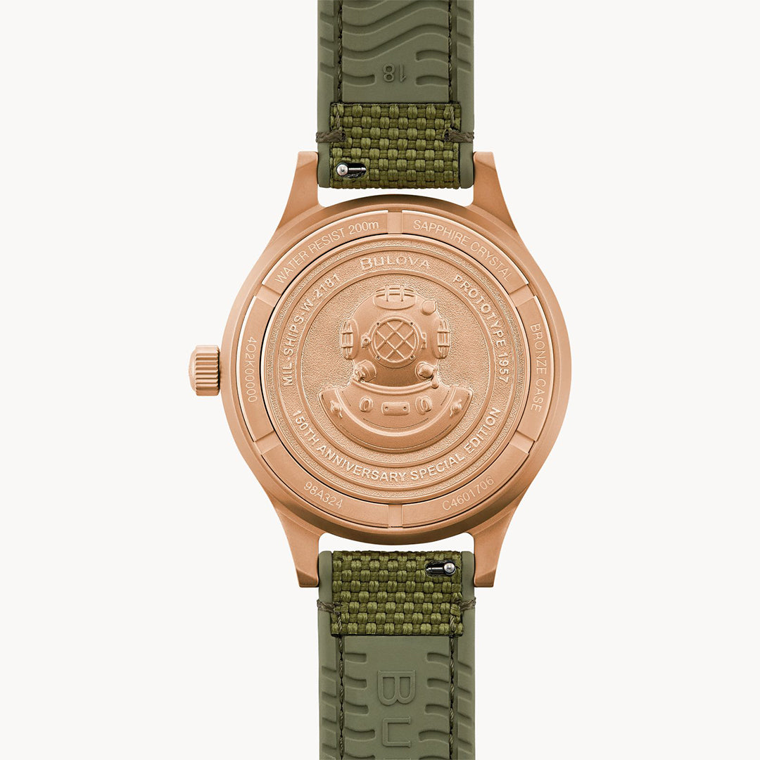 The back view of the Bulova Mil Ships Automatic 41mm watch shows engraved text with a deep-sea diving helmet design. Celebrating Bulova's 150th Anniversary, it features a U.S. Navy insignia and specs on a green textured strap.