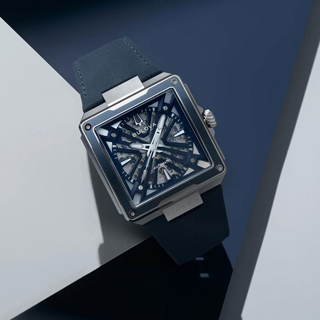A Bulova Series X Automatic 41mm watch is displayed at an angle on a geometric background with shadows, highlighting its square case, blue skeleton dial, and leather strap—a striking showcase of Bulova’s mastery in luxury automatic watchmaking.
