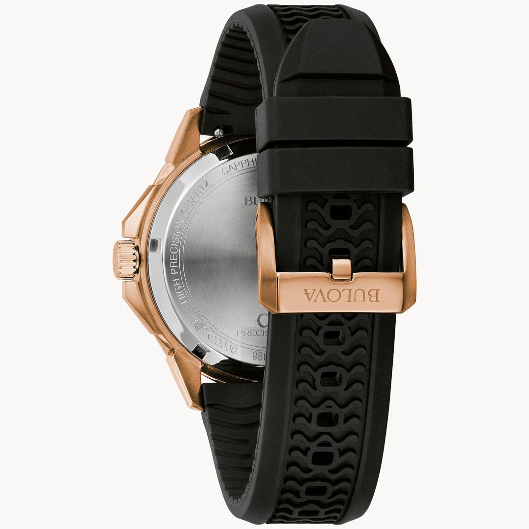 The image displays the back of the Bulova Marine Star Quartz 43mm Watch, which includes a black silicone strap with a gold-tone clasp. The round metallic back of the watch is engraved with text and has a crown situated on the side. The textured design of the strap enhances its sporty appearance, contributing to this stylish timepiece from Bulova.