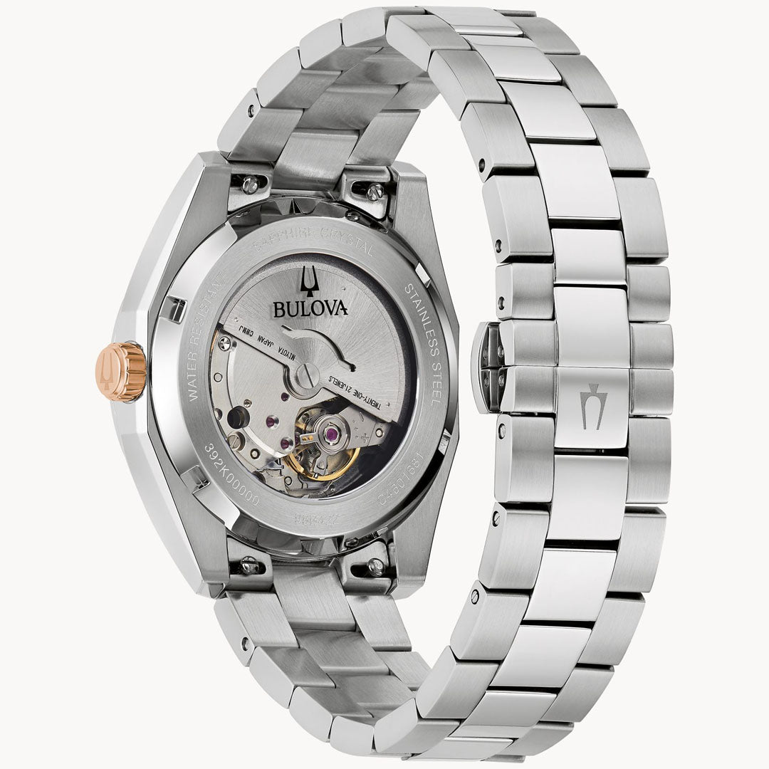 The Bulova Surveyor Automatic 39mm Watch showcases a sophisticated design with its silver stainless steel bracelet and transparent case back revealing the mechanical movement. It stands out with a captivating burgundy dial and an elegant rose gold crown. The back is intricately engraved with technical details and the Bulova logo, enhancing its refined appeal.