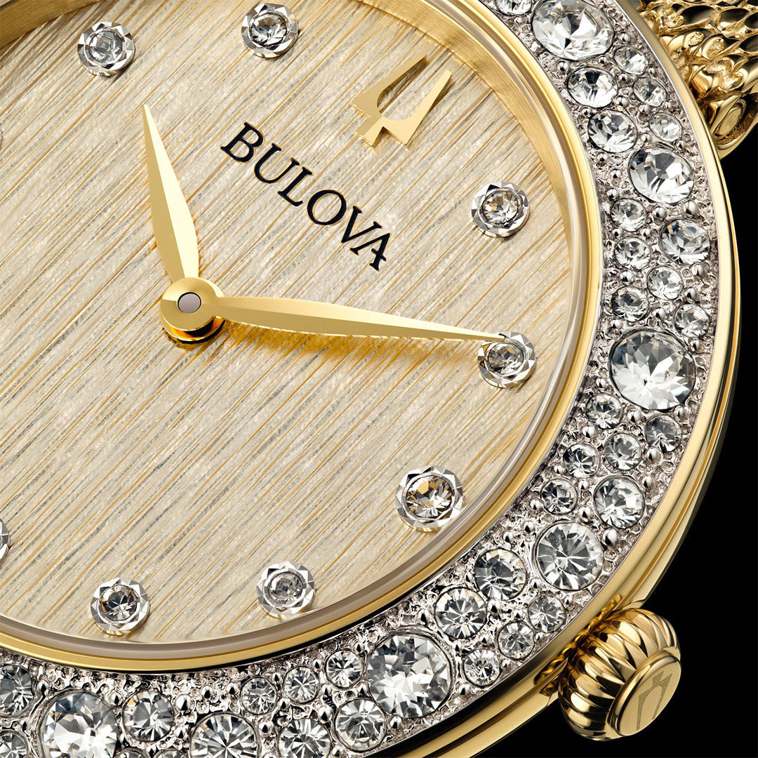 Close-up of the Bulova Crystal Quartz 32mm Watch, featuring a gold-tone stainless steel design, textured dial with Roman numeral "IV," gold hands, bezel adorned with Austrian crystals, decorative crown, and textured outer ring.