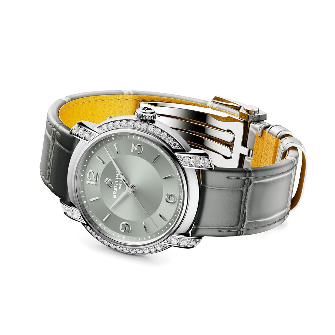 The Breitling Lady Premier Automatic 36 is a women’s silver watch featuring a diamond-studded bezel, gray leather strap, and light gray dial with silver markers and hands, displayed against a white background.
