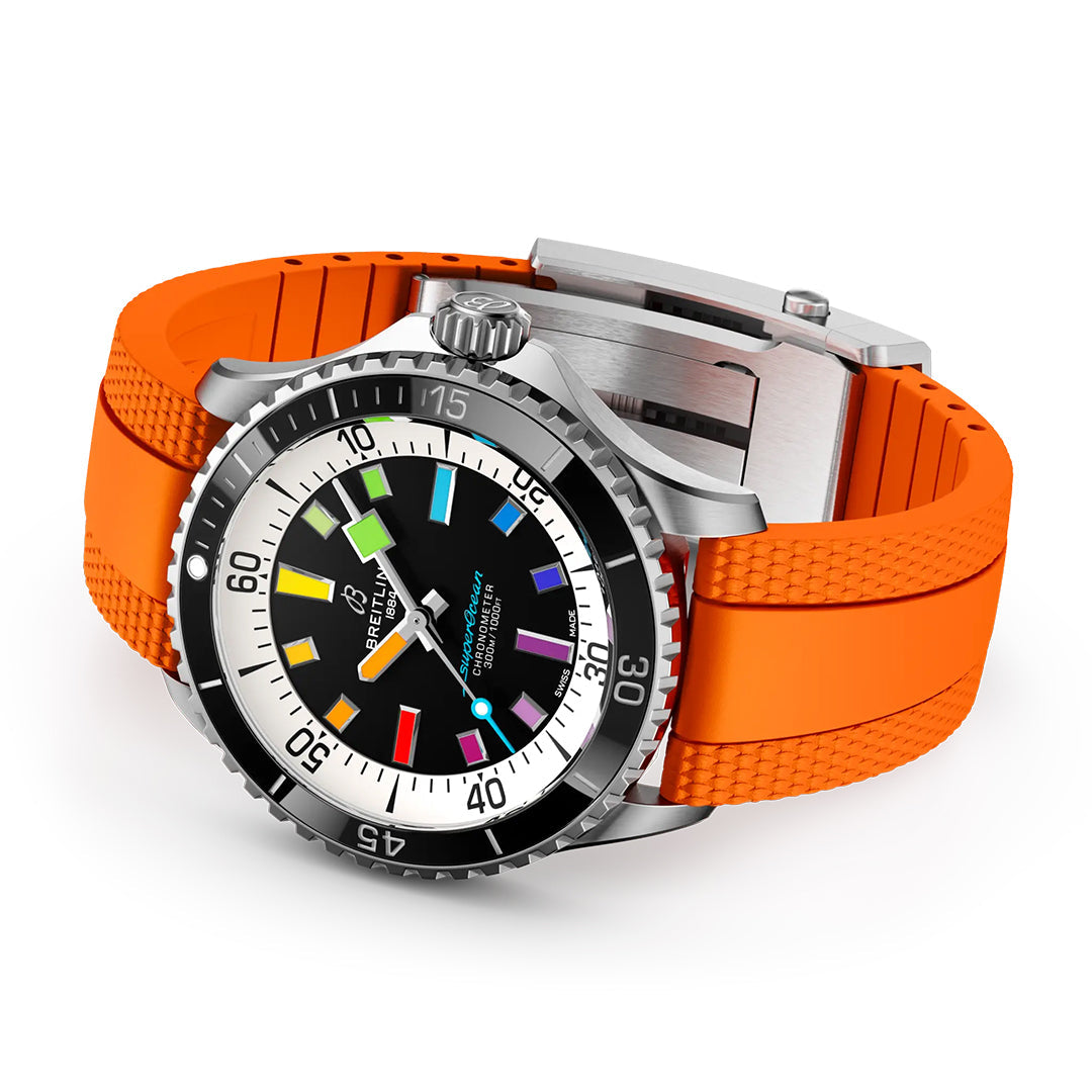 The BREITLING Superocean Automatic 42 by Breitling features a stainless steel case, black dial, white bezel, orange textured rubber strap, and colorful luminescent indexes. The watch is angled to highlight its bold face and strap.