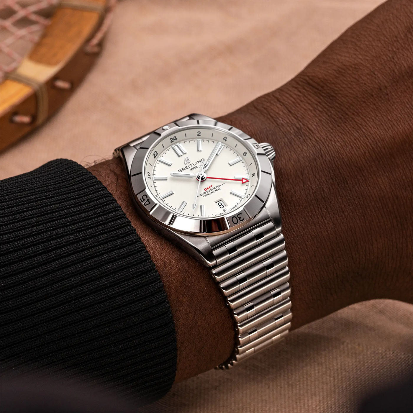 Close-up of a wrist adorned with the BREITLING Chronomat Automatic GMT 40, showcasing its stainless steel case, silver bezel, and white dial. This sophisticated Breitling timepiece features a date indicator and intricate black, red, and silver details. The person sports a black long-sleeve shirt for an elegant look.