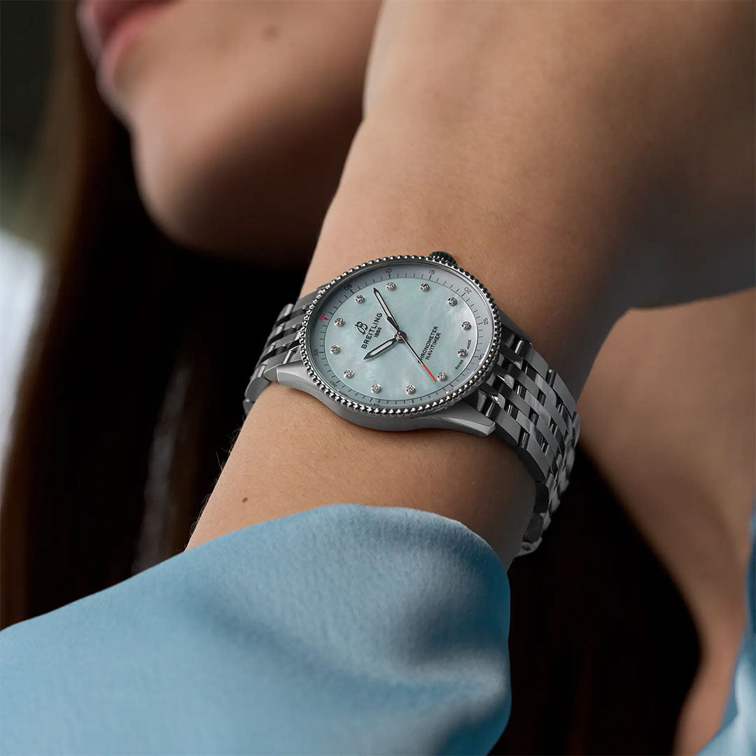 Someone wearing a Breitling Navitimer 32 luxury watch, featuring a silver case, white dial, and diamond markers, dressed in a light blue sleeve, rests their hand near their face.