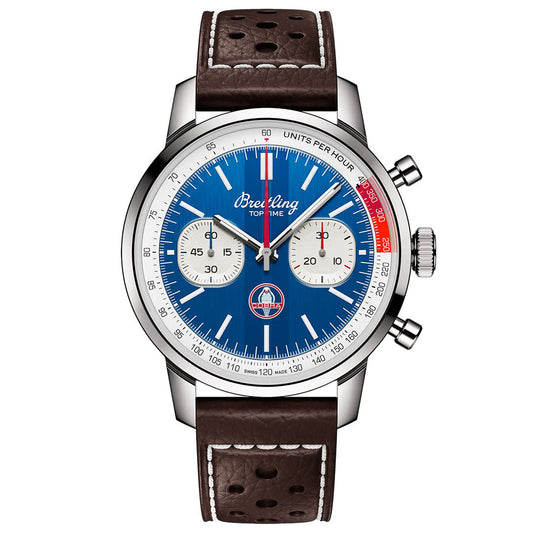 The Breitling Top Time B01 Shelby Cobra is a chronograph wristwatch featuring a blue dial, two white subdials, red and white accents, tachymeter scale, and a brown perforated leather strap. The "Top Time" logo appears on the face.