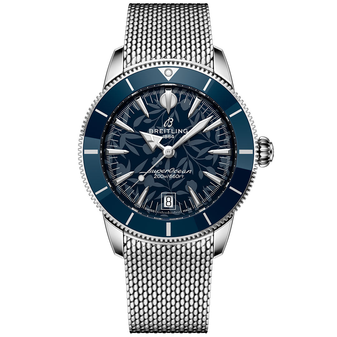 The BREITLING Superocean Heritage B31 Automatic Kelly Slater 40 is a silver wristwatch with a blue bezel, patterned blue dial, date at 6 o’clock, stainless steel mesh band, water-resistant to 200m, and features luminescent hands and markers.