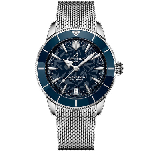 The BREITLING Superocean Heritage B31 Automatic Kelly Slater 40 is a silver wristwatch with a blue bezel, patterned blue dial, date at 6 o’clock, stainless steel mesh band, water-resistant to 200m, and features luminescent hands and markers.
