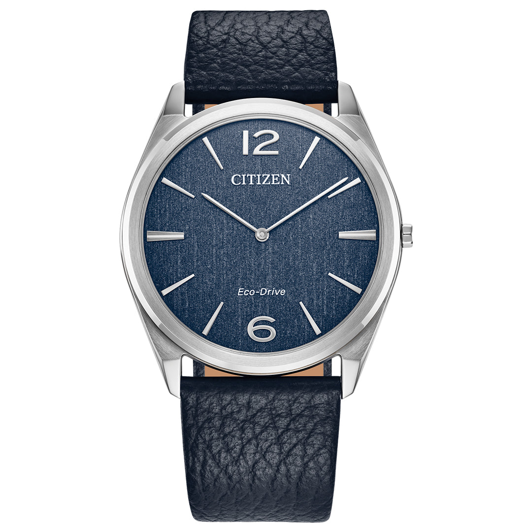 The CITIZEN Suratto Eco-Drive 38.4mm Watch, from the Classic Collection, features a sleek silver case and blue textured face with silver markers at 2, 4, 8, and 10 o'clock and bold numerals at 12 and 6. A dark blue leather band complements its refined appearance.