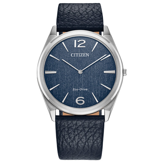 The CITIZEN Suratto Eco-Drive 38.4mm Watch, from the Classic Collection, features a sleek silver case and blue textured face with silver markers at 2, 4, 8, and 10 o'clock and bold numerals at 12 and 6. A dark blue leather band complements its refined appearance.