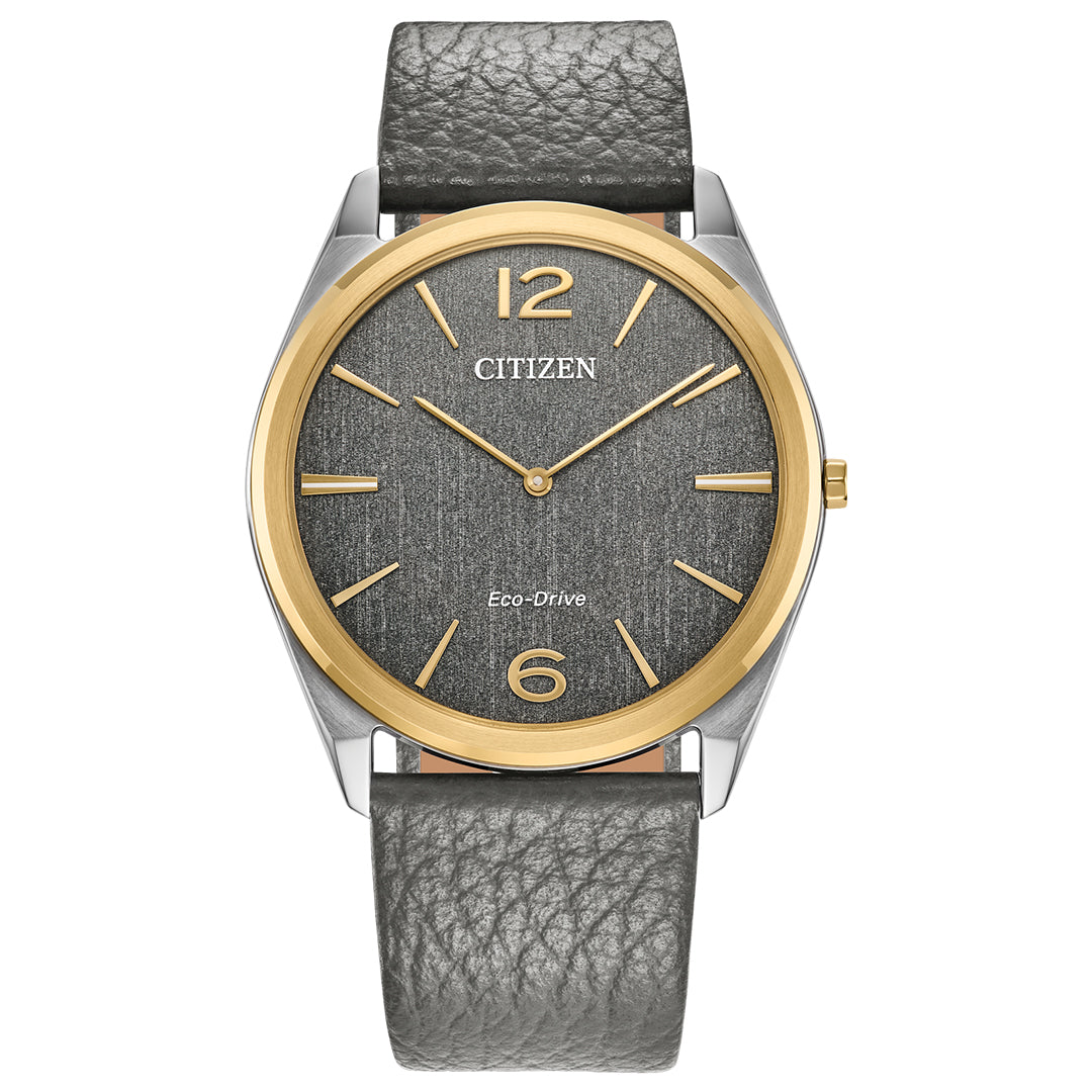 The CITIZEN Suratto Eco-Drive 38.4mm watch has a grey textured face and gold-tone hour markers, enclosed in two-tone stainless steel. It includes a grey leather strap, is water-resistant, and showcases elegance with its sustainable Eco-Drive technology.