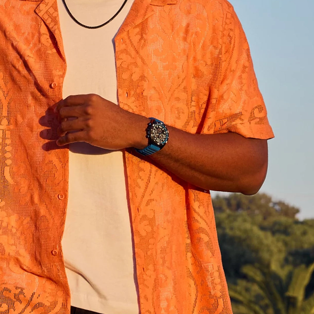 An individual in an orange patterned short-sleeve shirt over a white t-shirt showcases the CITIZEN Brycen Eco-Drive 44.8mm Watch outdoors, where the blurred greenery highlights its water-resistant design and advanced Eco-Drive technology.