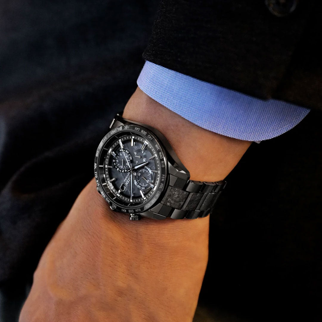 A person wearing a CITIZEN Attesa Hakuto-R Atomic Time Keeping Super Titanium Limited Edition Eco-Drive 42mm watch with a detailed multi-dial face and black band, paired with a dark jacket and light blue dress shirt.