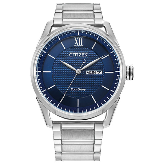 The CITIZEN Classic Eco-Drive 42mm Watch features a metallic silver band and casing, a blue textured dial with silver hour markers, and a Roman numeral at 12 o'clock. It displays the day and date on the right side and is water-resistant.