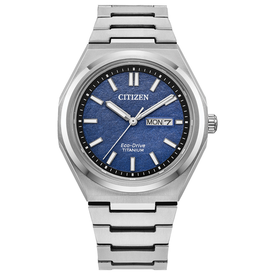 The CITIZEN Zenshin Three-hand Eco-Drive 39mm Watch features a stainless steel bracelet, blue textured dial with silver hour markers and hands, day-date display at 3 o'clock, and Eco-Drive technology for reliable power.