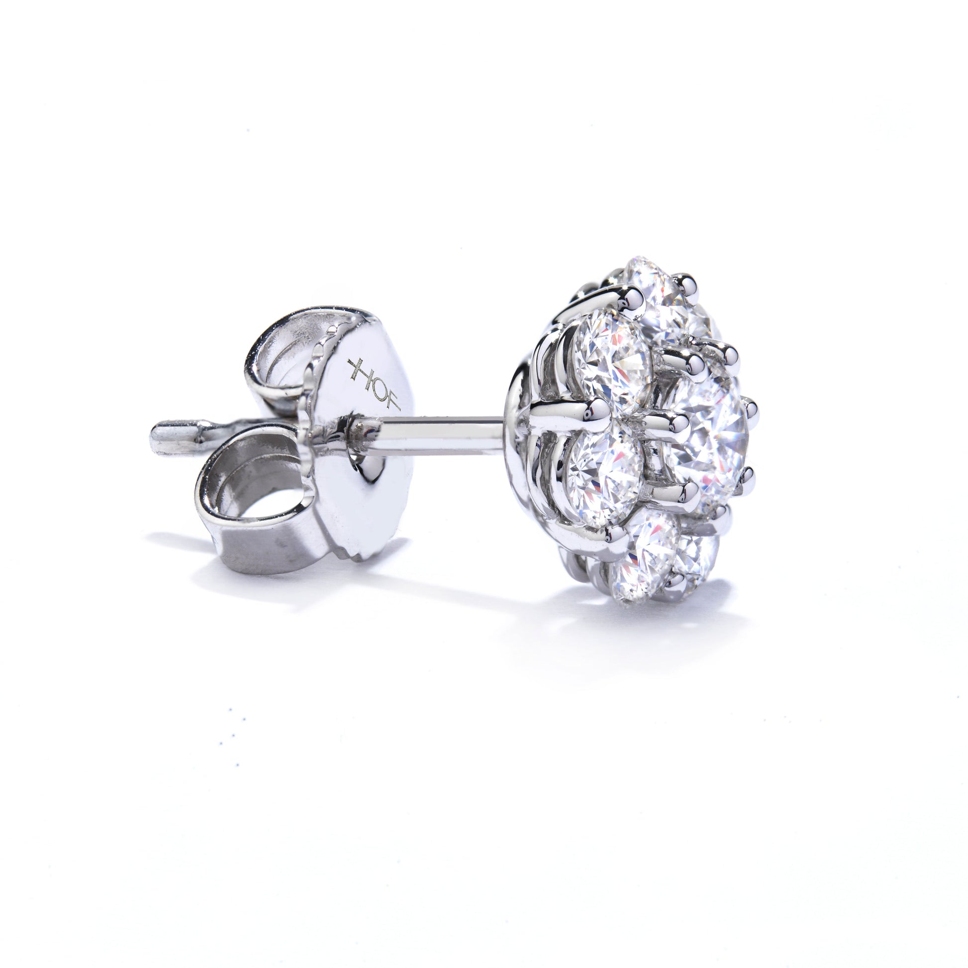 Displayed on a reflective white surface is the Hearts On Fire Beloved 18K White Gold Halo Stud Earring, featuring a cluster of round diamonds in a floral pattern. Crafted by Hearts On Fire, these earrings are completed with an 18 Karat White Gold setting and butterfly clasp.