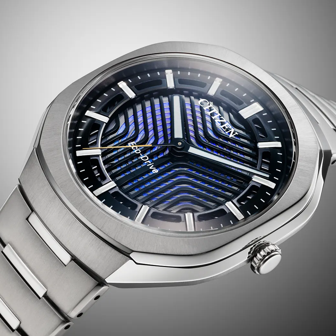 Close-up of the CITIZEN Photon Eco-Drive 39.6mm Limited Edition watch, featuring a silver metal band and a striking black and blue patterned dial, showcasing sport luxury against a gradient gray background.