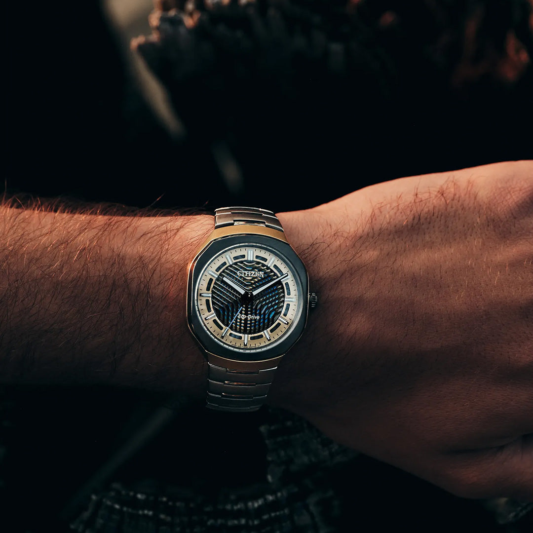 A close-up of a person’s wrist wearing the CITIZEN Photon Eco-Drive 39.6mm Watch, a limited edition silver metal timepiece with a black and silver patterned face, shown in warm lighting.