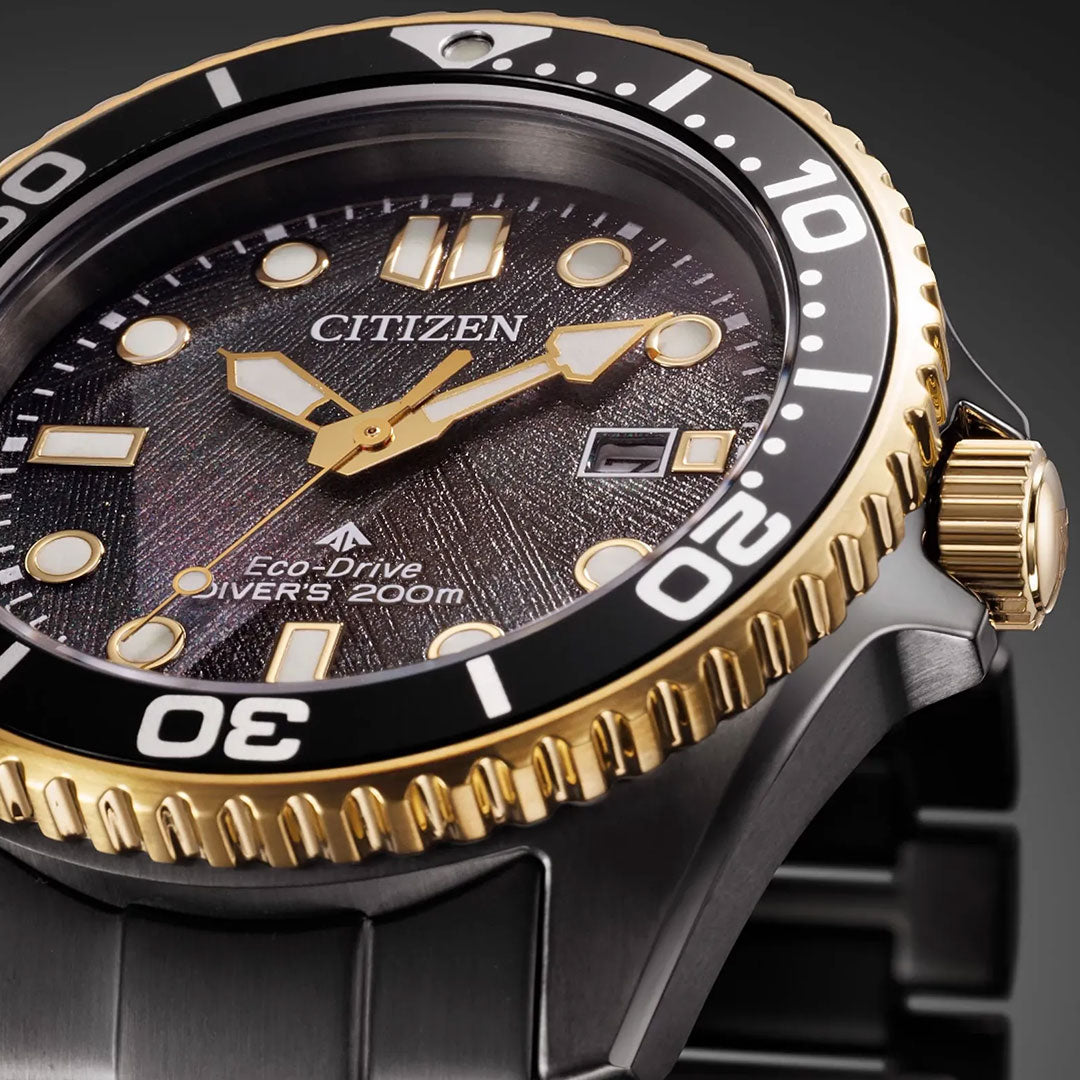 Close-up of the CITIZEN Promaster Dive Light in Black Eco-Drive 40.6mm, featuring a textured black dial, gold and black bezel, luminescent markers, stainless steel band, and 200m water resistance.
