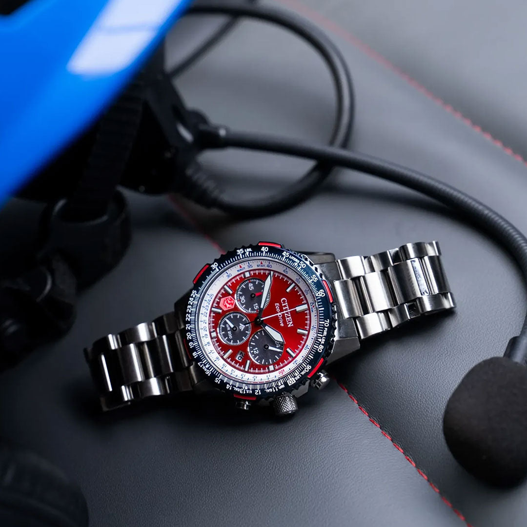 The CITIZEN Promaster Navihawk Eco-Drive 40mm Watch sits on a gray leather seat with red stitching, beside a black headset and a blue object—likely a Royal Canadian Air Force helmet.