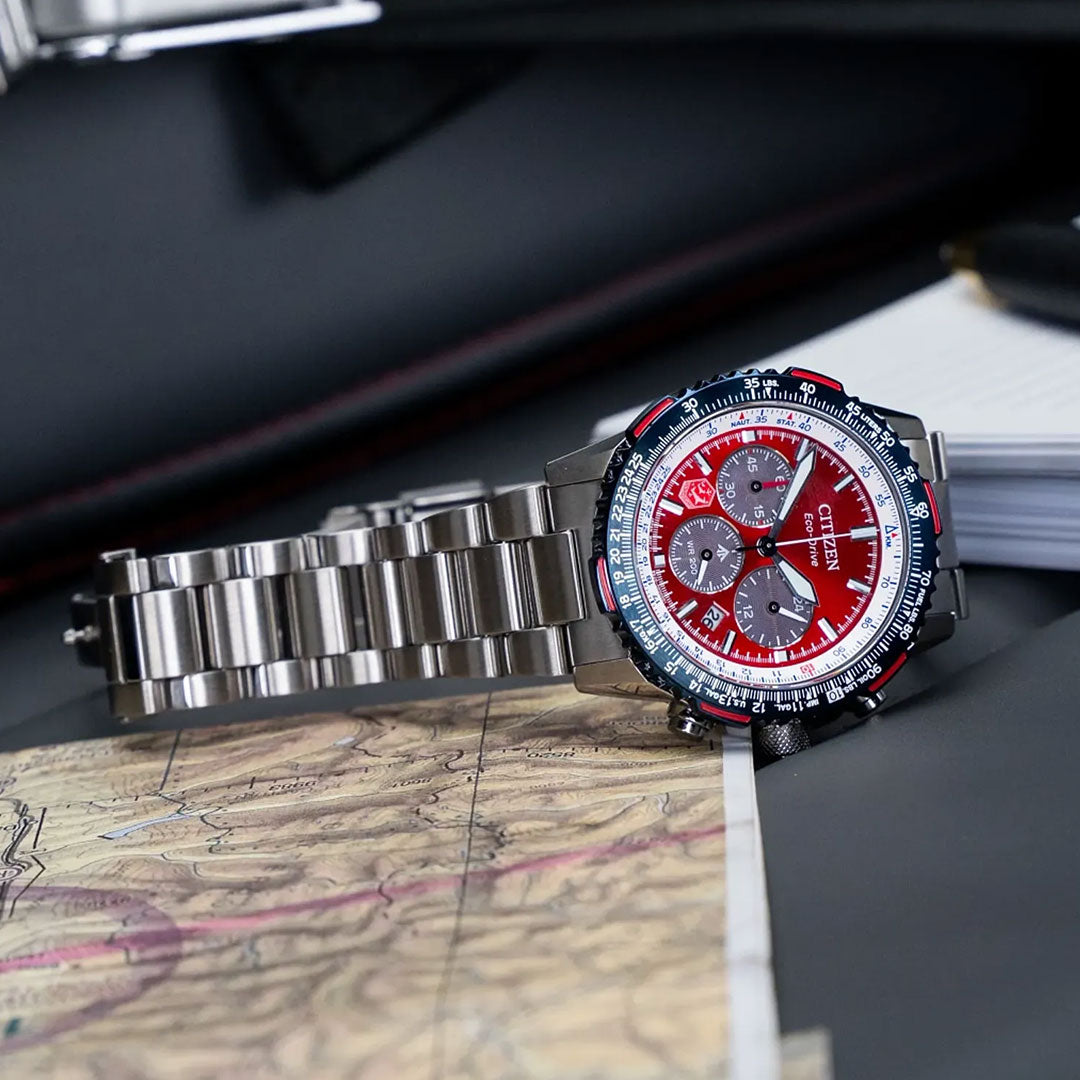 A CITIZEN Promaster Navihawk Eco-Drive 40mm watch with a red and blue dial and three subdials rests on a map, with a notebook and pen in the background—a stylish tribute to the Royal Canadian Air Force.