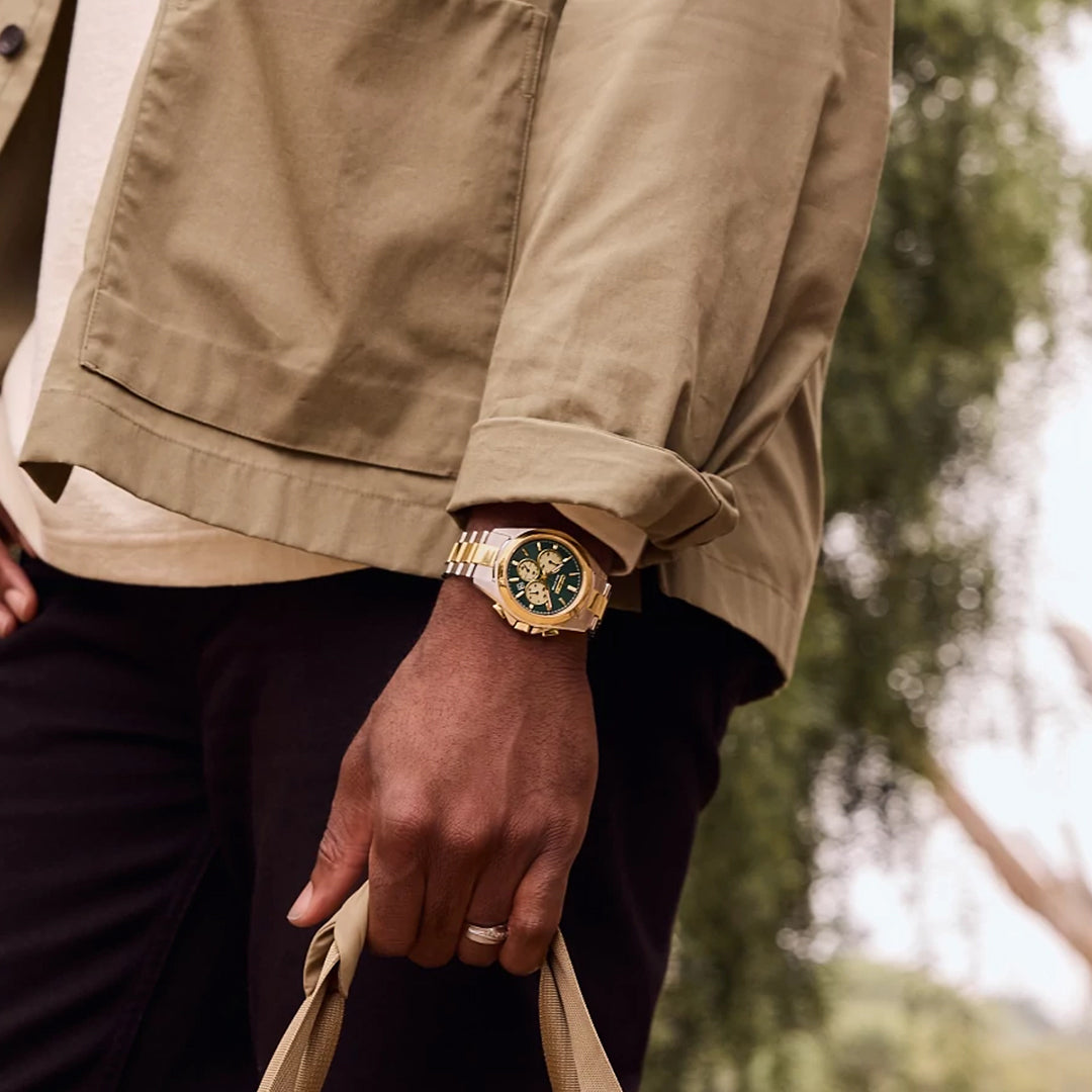 A person in a light brown jacket is seen from the side, showcasing their wrist adorned with a CITIZEN Sport Luxury Eco-Drive 40.5mm watch featuring a black face. They hold a beige bag handle against a blurred outdoor backdrop, exuding sophisticated charm.