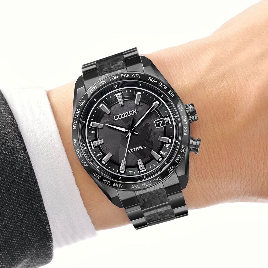 A close-up of a wrist adorned with the CITIZEN Attesa Hakuto-R Atomic Time Keeping Super Titanium Limited Edition Eco-Drive 40.6mm watch, featuring a round black dial and city codes bezel, worn with a white shirt and dark suit jacket.