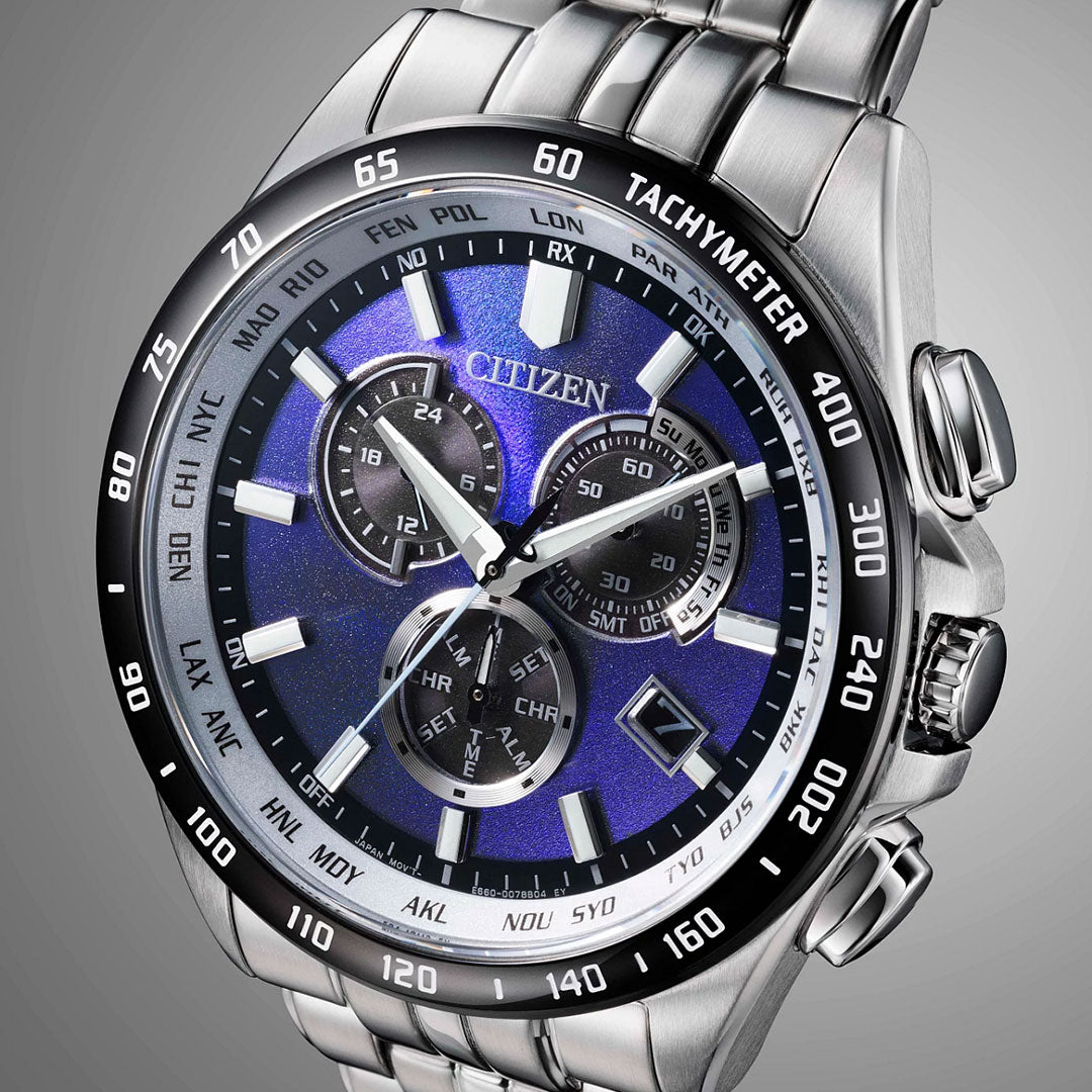 A close-up of the CITIZEN Perpetual Chrono A-T Eco-Drive 43mm Watch shows a blue dial, silver hour markers, subdials, date window, tachymeter on the black bezel, and a stainless steel bracelet.