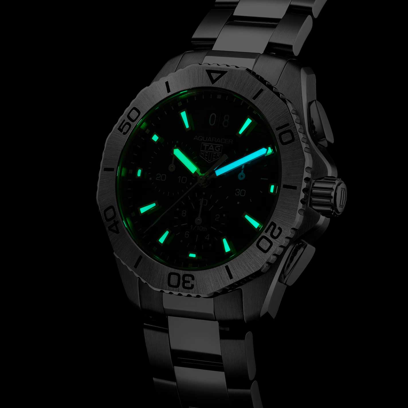 A close-up of the TAG Heuer Aquaracer Professional 200 Chronograph Quartz 40mm Watch in the dark, showcasing luminous green hour markers and hands with a distinctive blue second hand, all set on a stainless steel bracelet. The durable steel case emphasizes its exceptional water resistance, blending the iconic style and robust functionality that TAG Heuer is known for—perfect for any adventure.