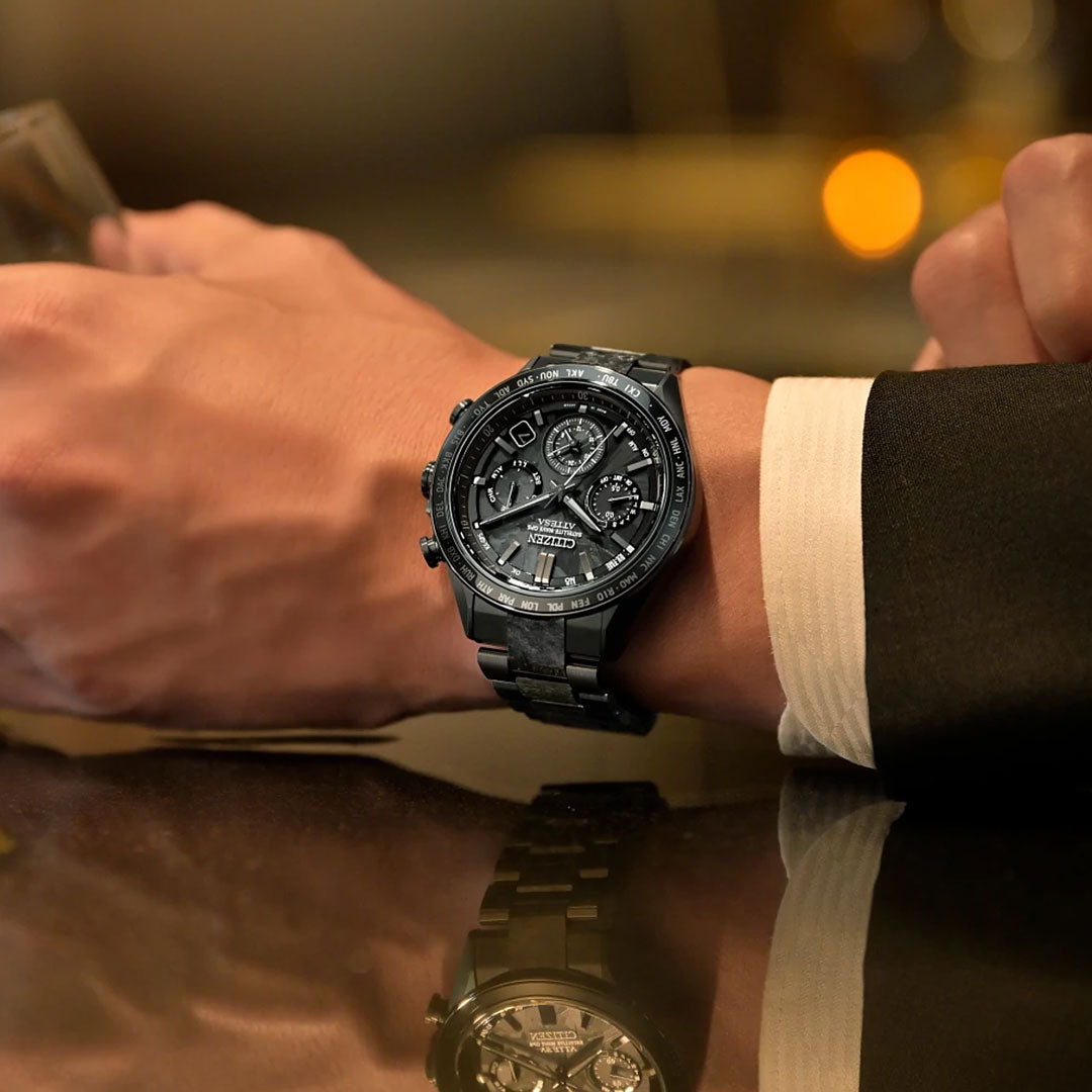 A person in a black suit rests their arm on a reflective surface, wearing the CITIZEN Attesa Hakuto-R Atomic Time Keeping Super Titanium Limited Edition Eco-Drive 44.6mm watch, featuring multiple dials and intricate design elements.