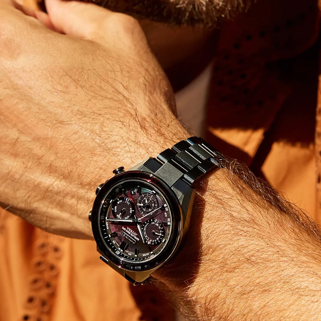 A close-up showcases a person’s wrist adorned with the CITIZEN Attesa Satellite Time Keeping Super Titanium Limited Edition Eco-Drive 44.6mm Watch, its striking black metal design with multiple dials standing out against an orange textured shirt. Crafted from Super Titanium, the CITIZEN timepiece embodies both strength and elegance as the wearer’s hand rests thoughtfully near their face.