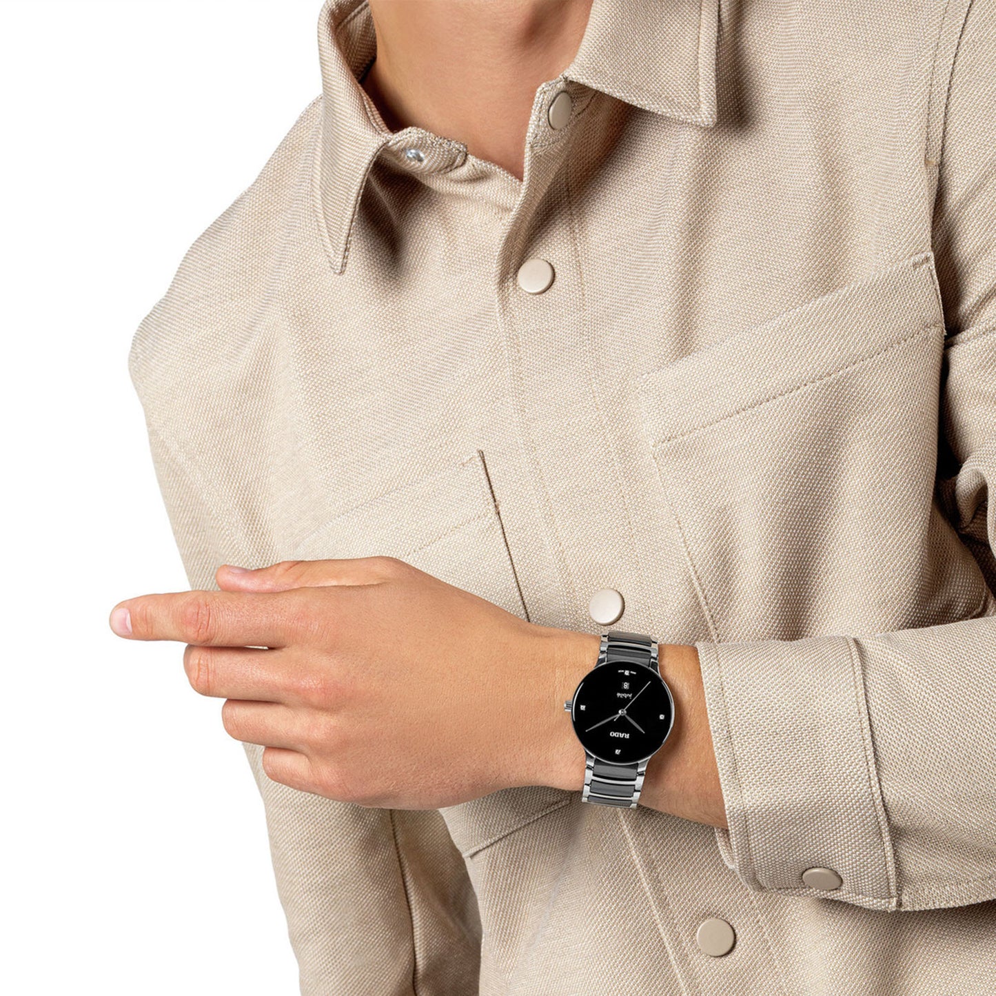 A person wearing a beige shirt gestures to the left, highlighting the high-tech RADO Centrix Diamonds Quartz 39.5mm Watch on their wrist. The silver timepiece boasts a black, round face and showcases precise PreciDrive technology, while the person's face is not visible.