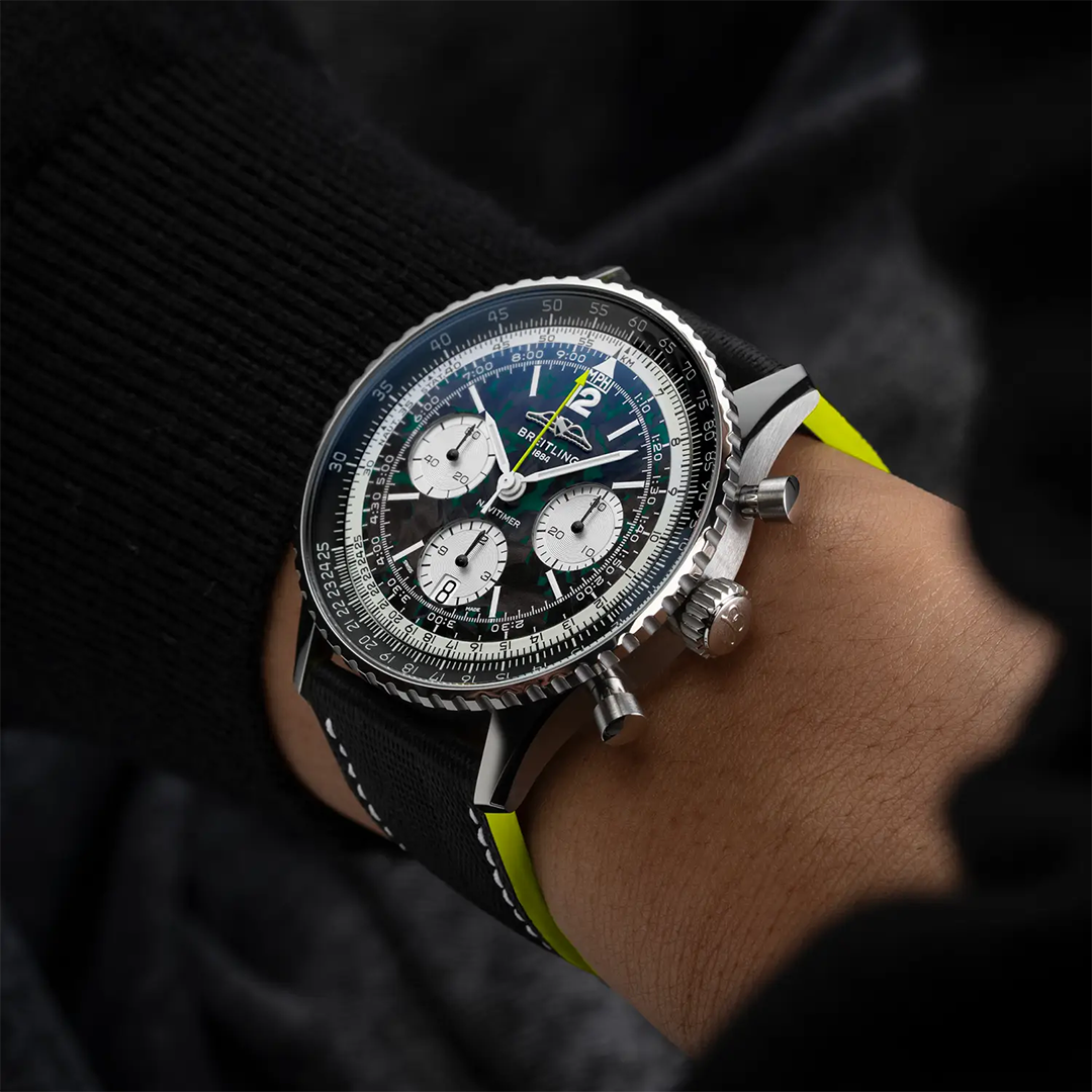 The BREITLING Navitimer B01 Chronograph 43 Aston Martin Aramco Formula One Team Edition with a dark green dial, three white subdials, a slide rule bezel, and a black strap with bright green edges worn on a wrist.