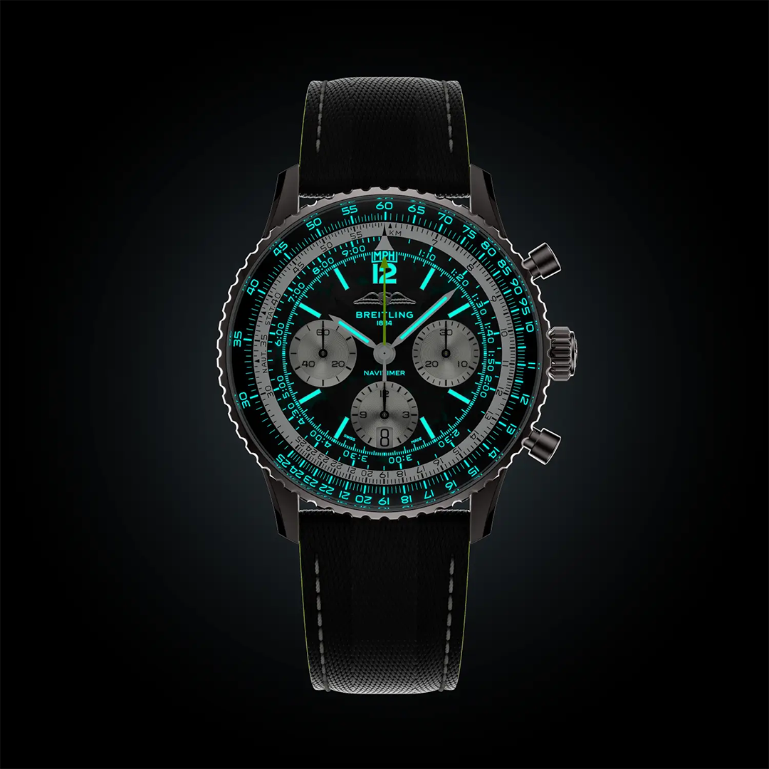 BREITLING Navitimer B01 Chronograph 43 Aston Martin Aramco Formula One Team Edition with a black dial, three silver sub-dials, and luminous teal accents on the hands, indices, and bezel against a black background.