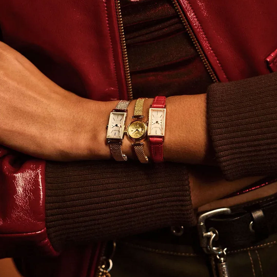A person in a red leather jacket crosses their arms, showing three wristwatches on one wrist: two rectangular stainless steel watches and a round CITIZEN Fio Eco-Drive 14.3mm Watch with a red leather band.