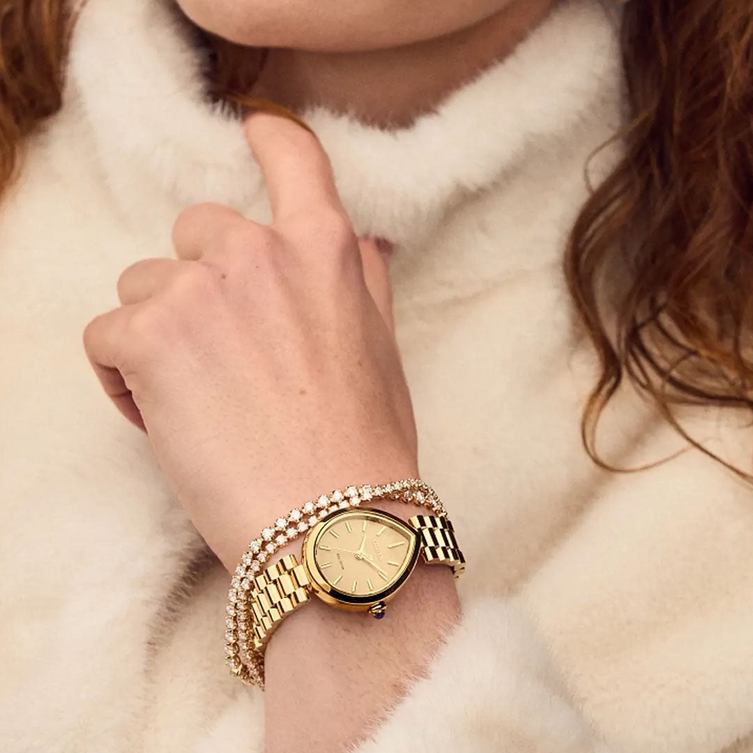 A person in a cream fuzzy sweater wears a CITIZEN L Rainell Eco-Drive 26mm women’s watch and a gold bracelet with sparkling stones. Only their lower face, hand, and some wavy brown hair are visible.