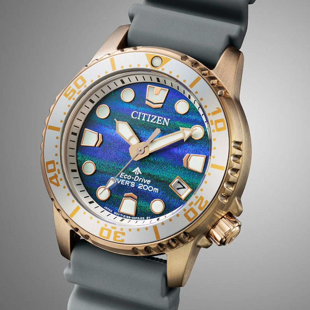 The CITIZEN Promaster Dive Eco-Drive 36.5mm Watch Limited Edition features a gold-tone case, blue and green textured dial, white bezel with gold accents, bold markers, gray strap, and is water-resistant up to 200 meters.