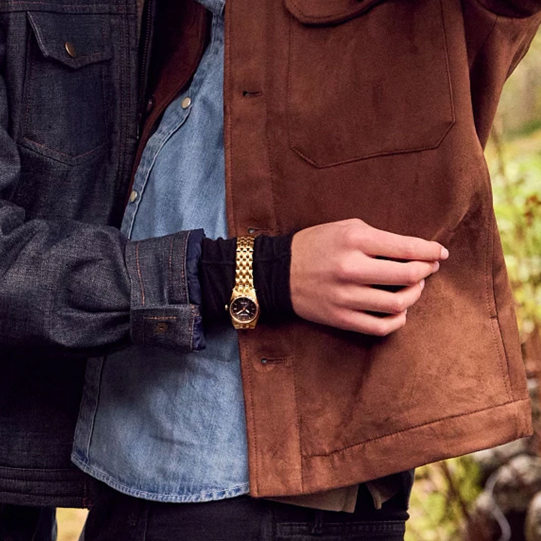 Someone wearing a CITIZEN Corso Eco-Drive 27mm Watch, a denim shirt, and brown jacket holds another person dressed in a dark denim jacket and light denim shirt. Only their torsos and arms are shown.