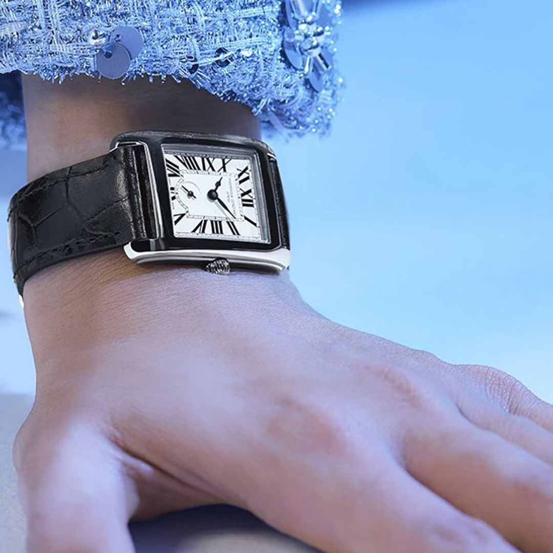 The image captures a close-up of a person's wrist adorned with the Frederique Constant Classics Carree Small Seconds Quartz 36mm x 25mm Watch. This luxury timepiece features a square face adorned with Roman numerals and includes small seconds. The black leather strap perfectly complements their textured blue attire, set against a softly blurred blue background.