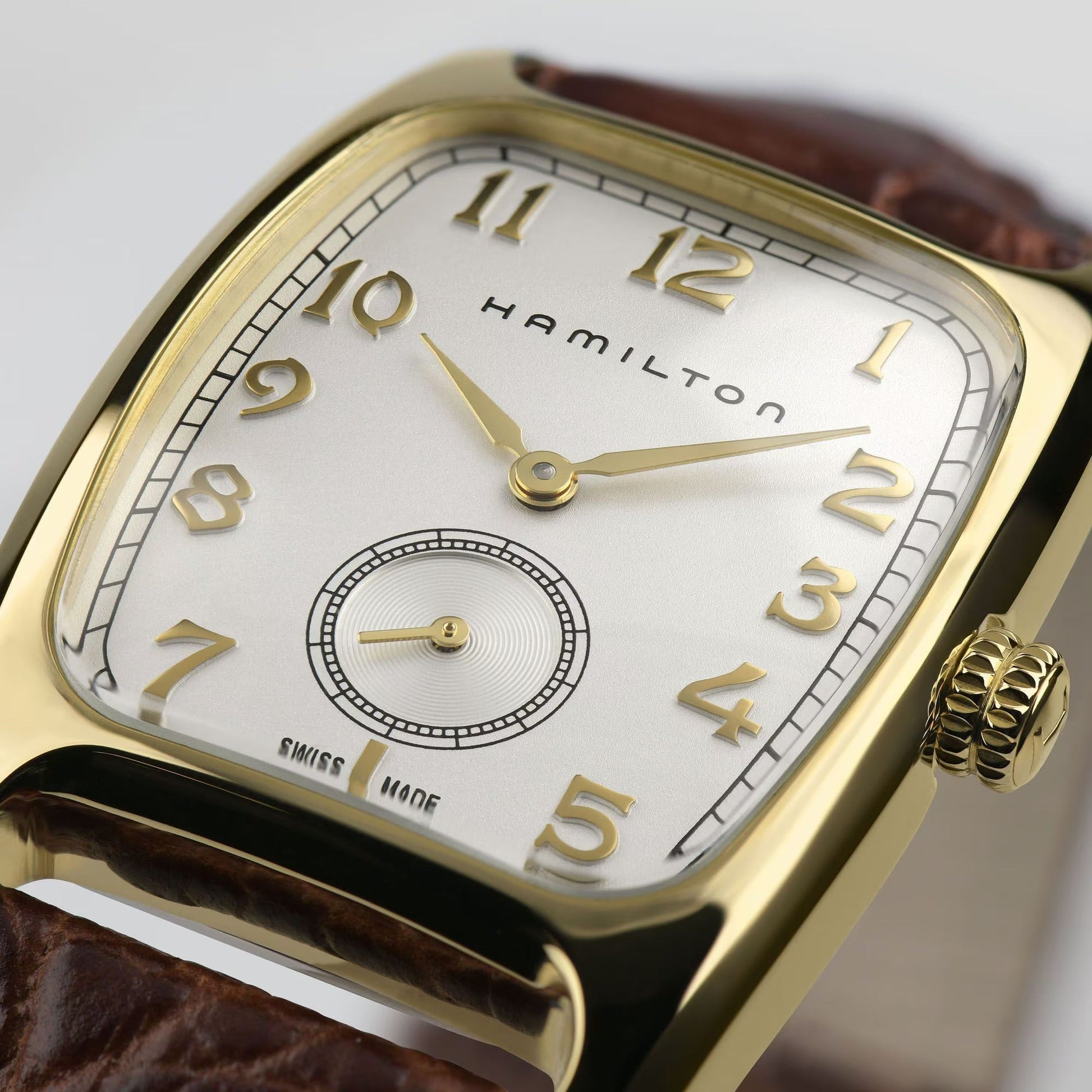 A close-up of the Hamilton American Classic Boulton Quartz 27mm x 32mm by Hamilton Watch, featuring a gold rectangular case, brown leather strap, white dial with gold Arabic numerals, and a small seconds subdial above 6 o'clock.