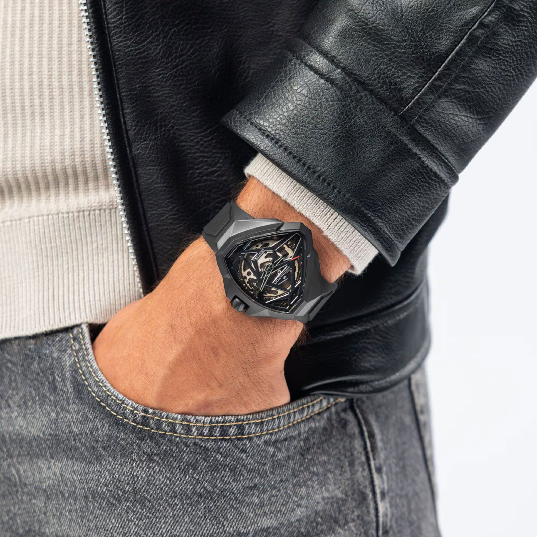 A person in a black leather jacket and jeans, hand in pocket, shows off a Hamilton Ventura Edge Skeleton Automatic 51mm x 47mm Watch by Hamilton Watch, featuring an angular case and skeletonized dial revealing its H-10-S movement.