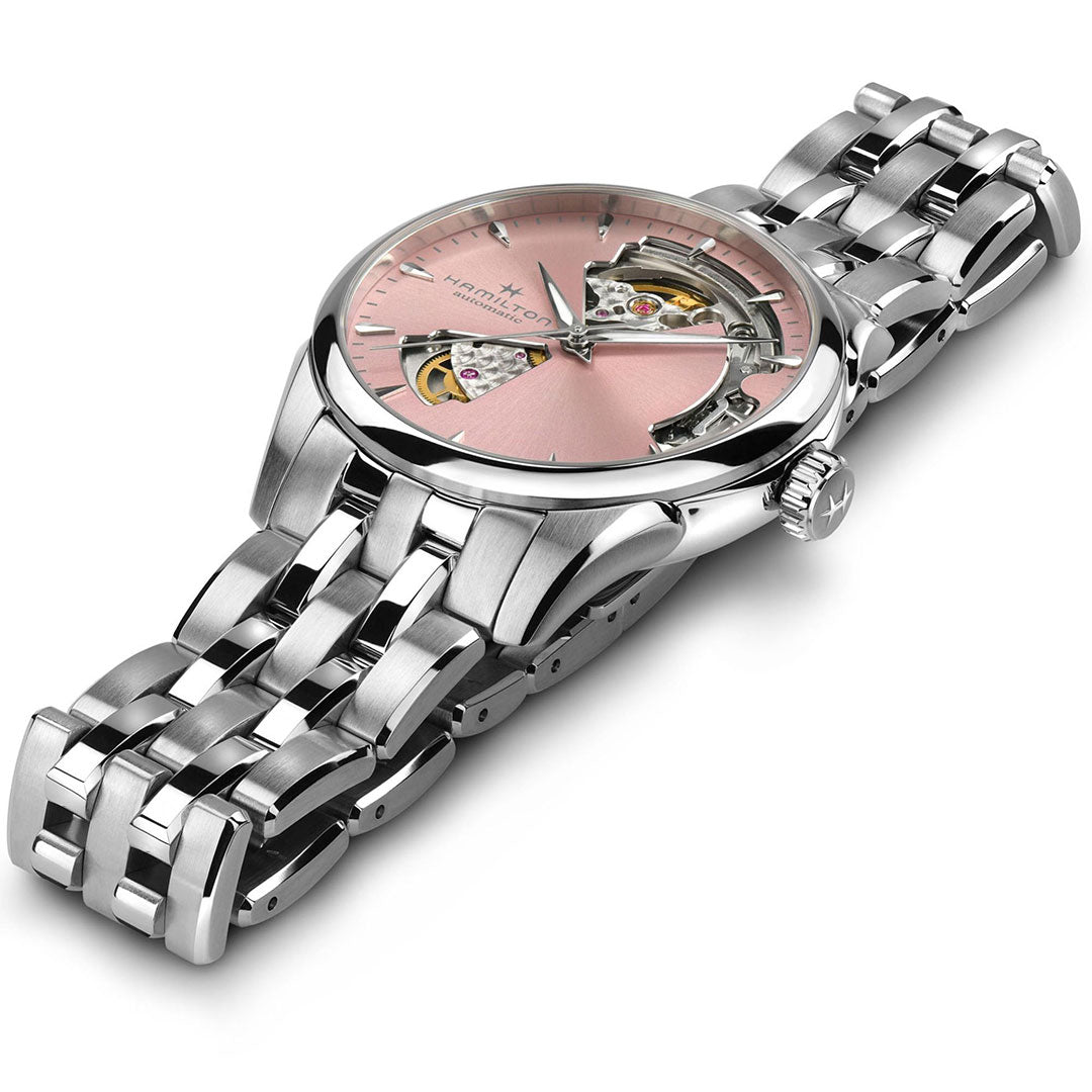 The Hamilton Jazzmaster Open Heart Auto 36mm Watch by Hamilton Watch features a stainless steel case, pink dial, and partially open face showing its mechanical movement, displayed at an angle against a white background.