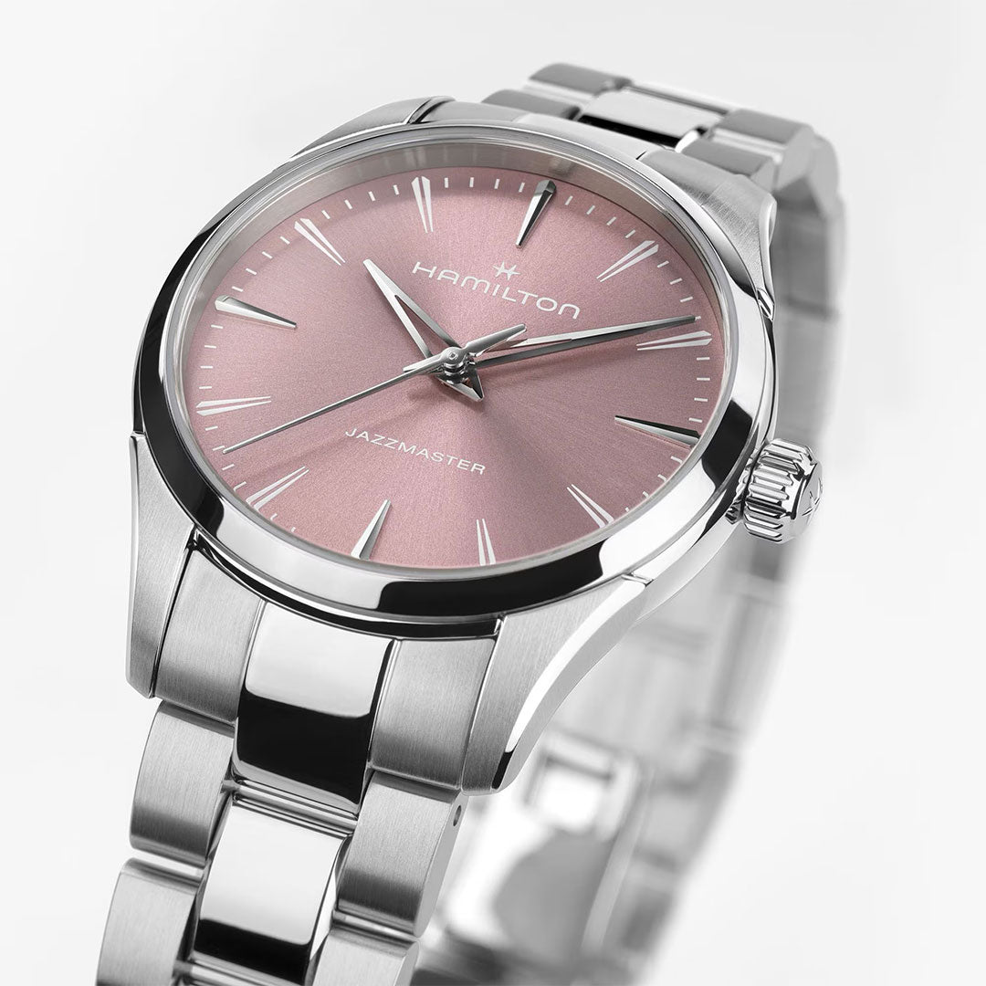 A close-up of the Hamilton Jazzmaster Quartz 32mm Watch by Hamilton Watch, showcasing its metallic silver band and pink sunburst dial with silver markers and hands, set against a white background.