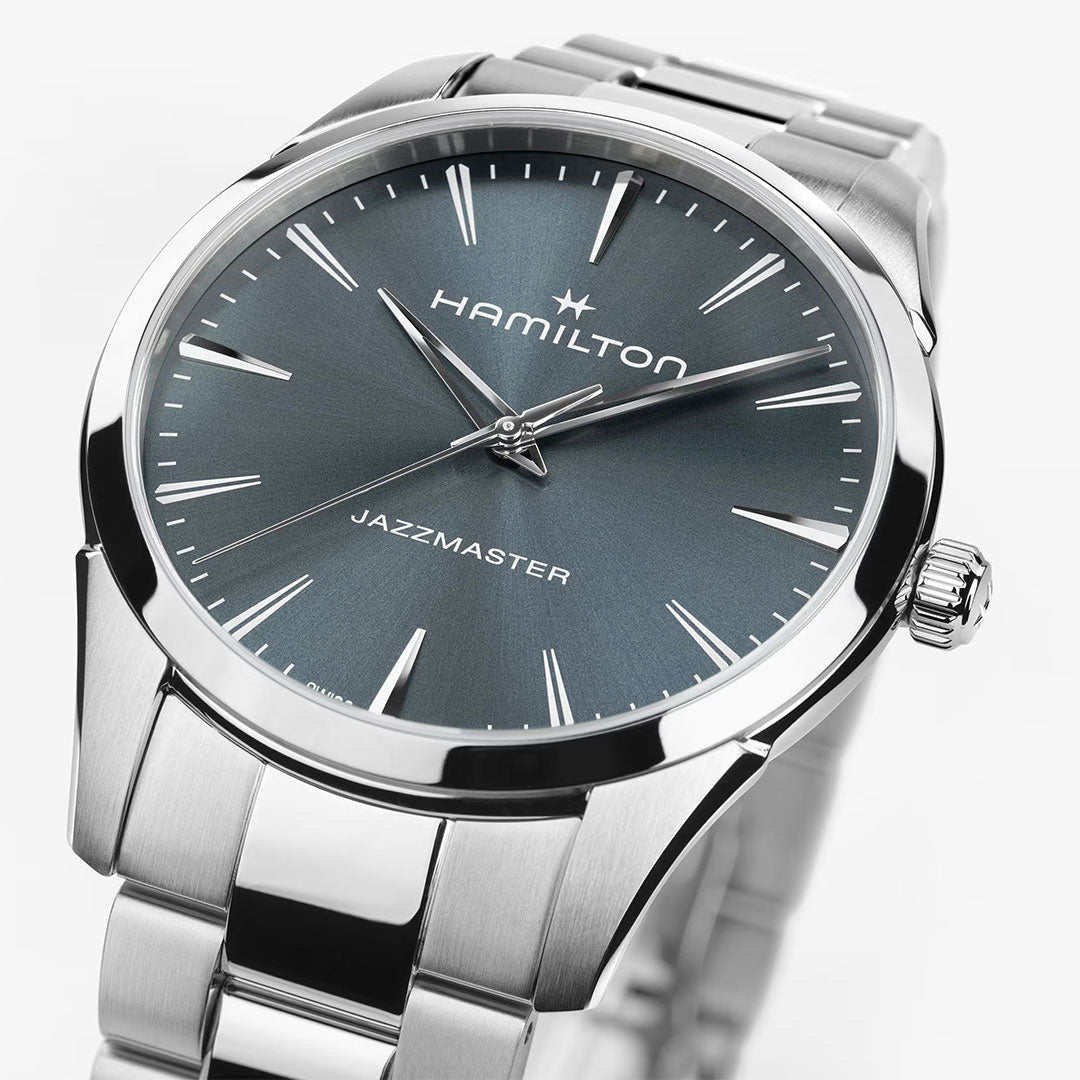 A close-up of the Hamilton Watch Jazzmaster Quartz 40mm, featuring a stainless steel band and blue-gray dial with silver markers and hands, photographed on a white background.