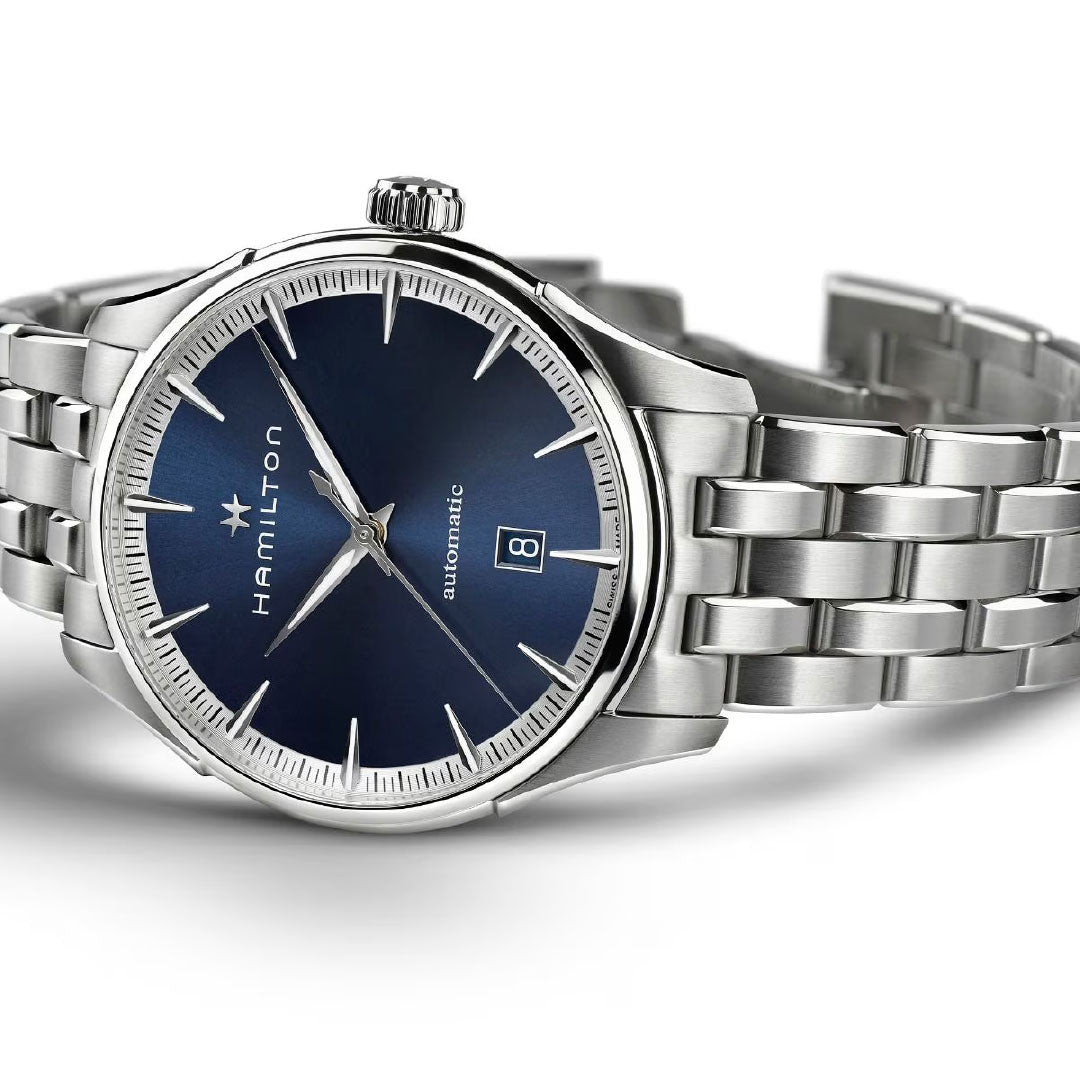 The Hamilton Jazzmaster Auto 40mm Watch by Hamilton Watch features a blue dial with silver markers and hands, date at 3 o’clock, and an anti-magnetic stainless steel bracelet, shown angled.