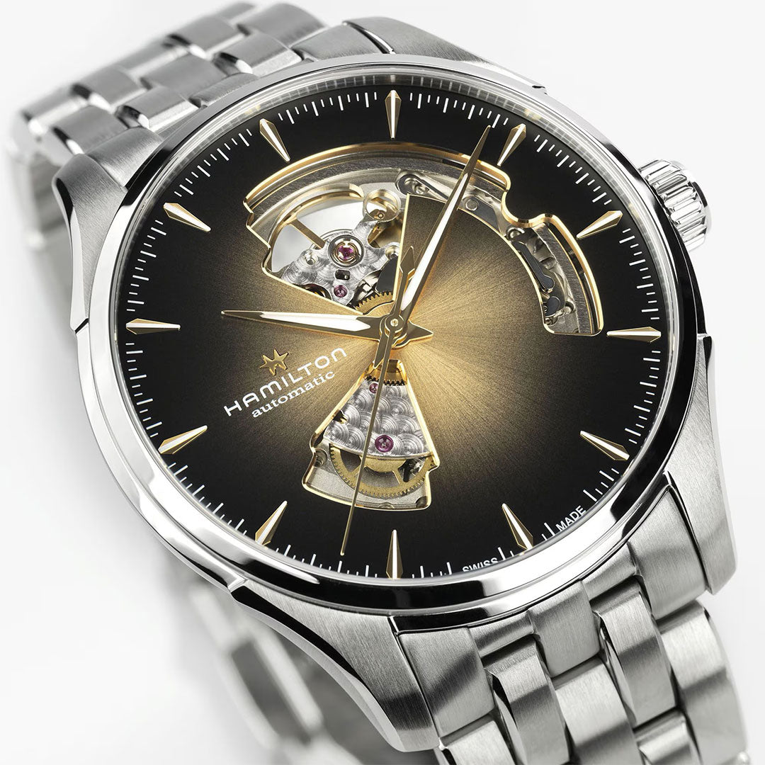A close-up of the Hamilton Jazzmaster Open Heart Auto 40mm by Hamilton Watch, featuring a black and gold sunburst dial with open sections showing the movement and a brown leather strap.