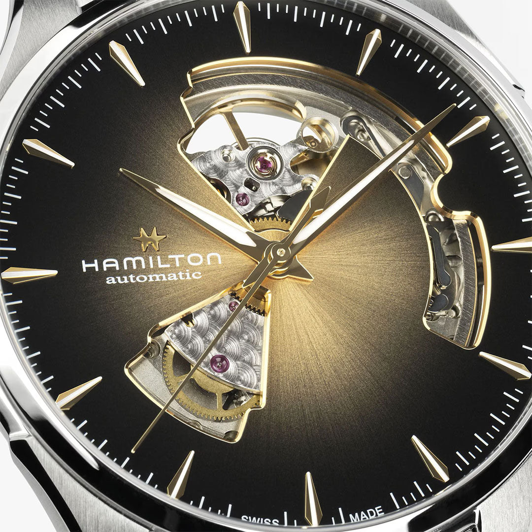 Close-up of the Hamilton Watch Jazzmaster Open Heart Auto 40mm, featuring a black and gold gradient dial with visible automatic movement, gold hour markers and hands, exposed gears, and a brown leather strap for an intricate look.